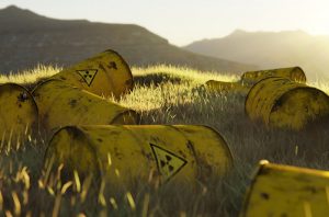 Gelbe Fässer mit Warnhinweisen auf nuklearen Inhalt liegen im Gras in der aufgehenden Sonne